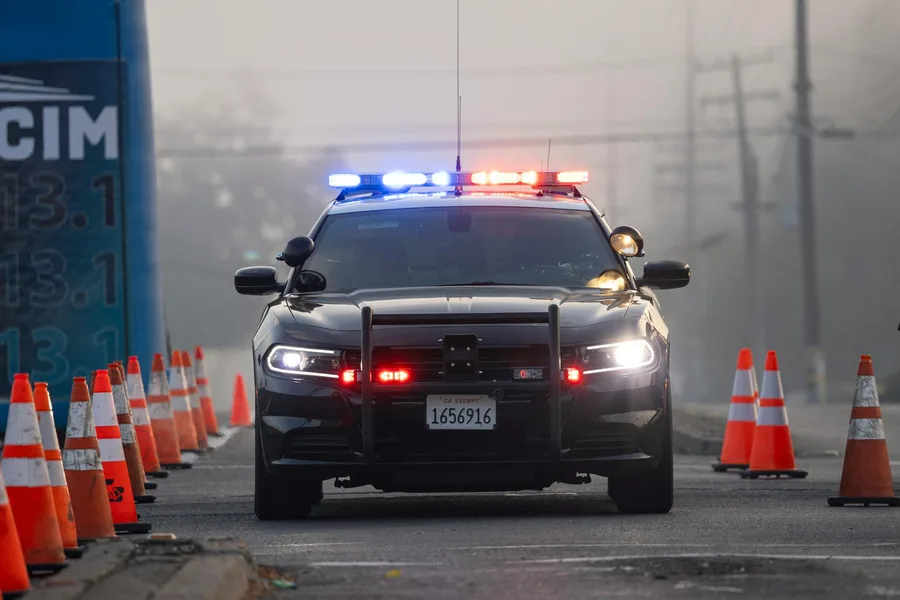 A police car with sirens on at a traffic checkpoint surrounded by cones.