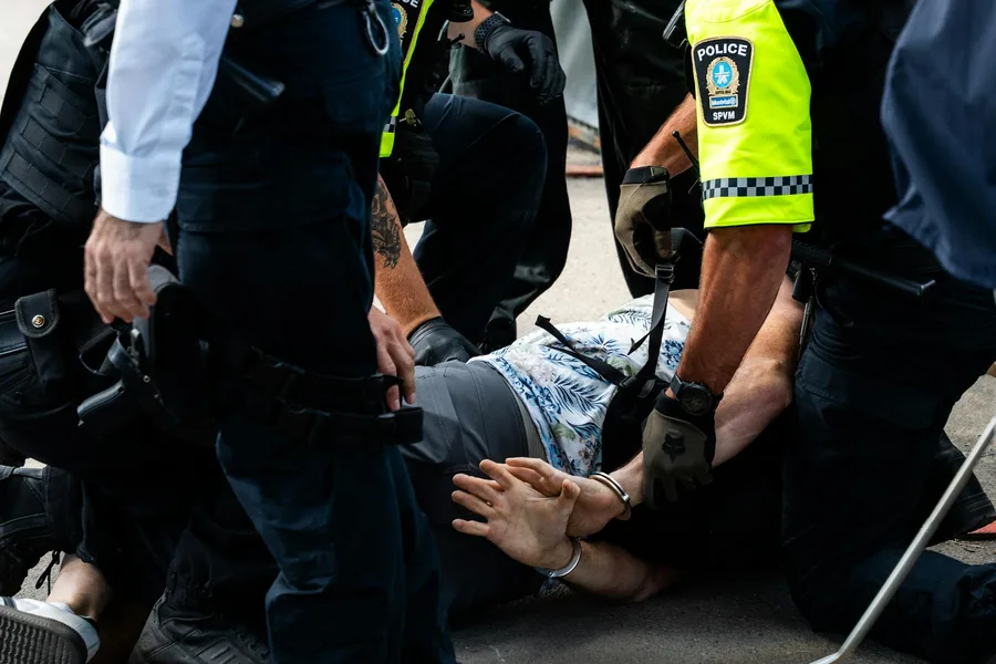Multiple police officers detain a person on a city street, using handcuffs to restrain them.