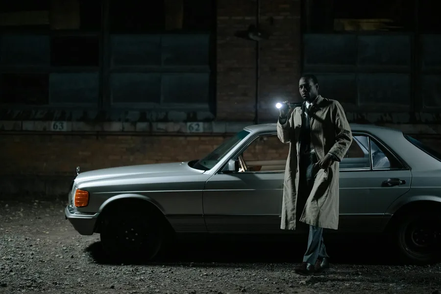 Detective conducting a night investigation by a car with a flashlight.