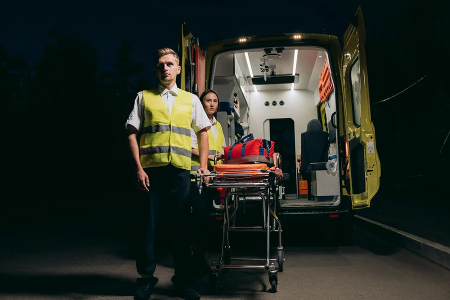 Paramedics with stretcher beside ambulance at night, ready for emergency care.