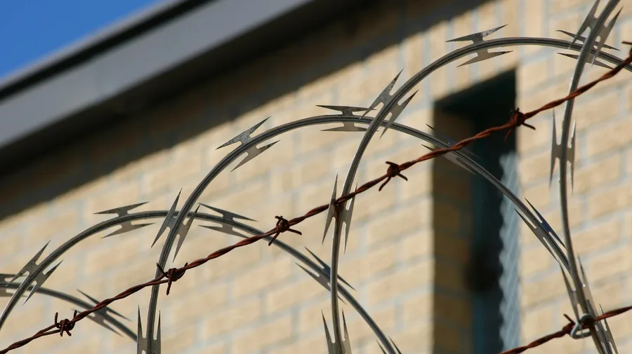 Sharp barbed wire in focus with a blurred brick wall background.