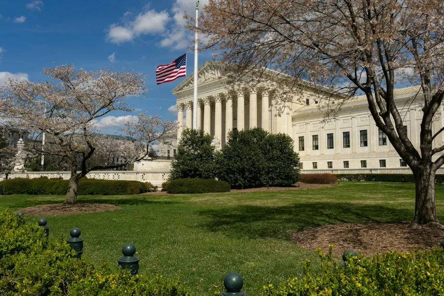 A view of a neoclassical government building with an American flag and cherry blossoms in Washington, DC.