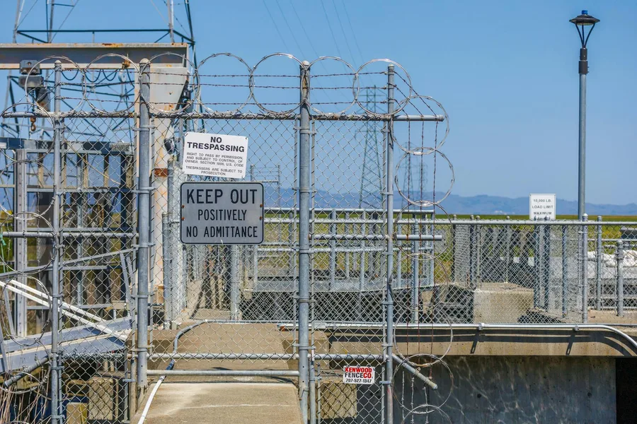 Image of a secure fenced area with multiple keep out and no trespassing signs and barbed wire.
