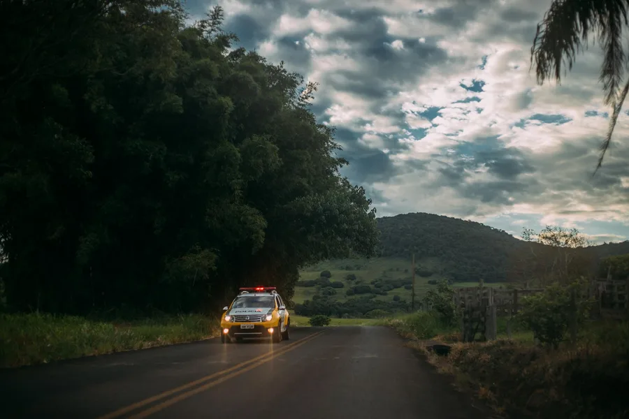 A police car drives on a rural road against a scenic twilight sky.
