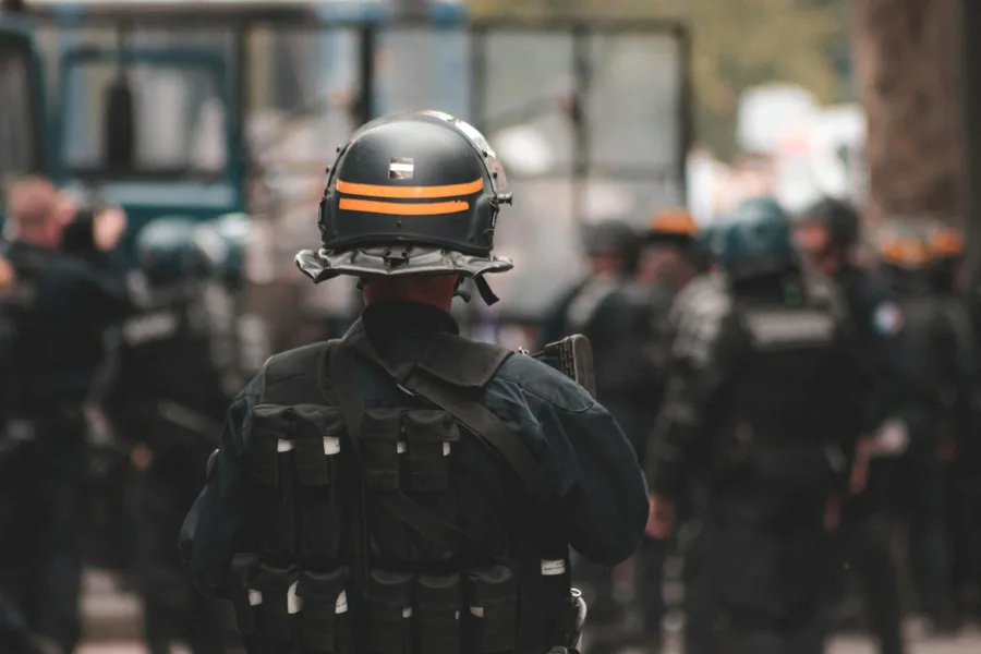 Back view of anonymous policeman in helmet and bulletproof vest maintaining law and order while standing on city street