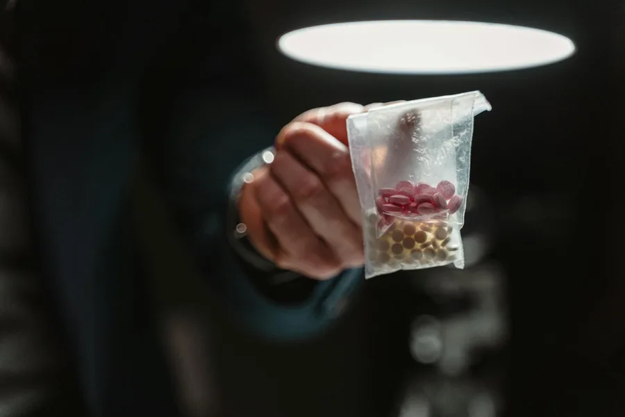 Close-up view of a hand holding a bag of assorted pills under stark lighting, conveying a serious tone.
