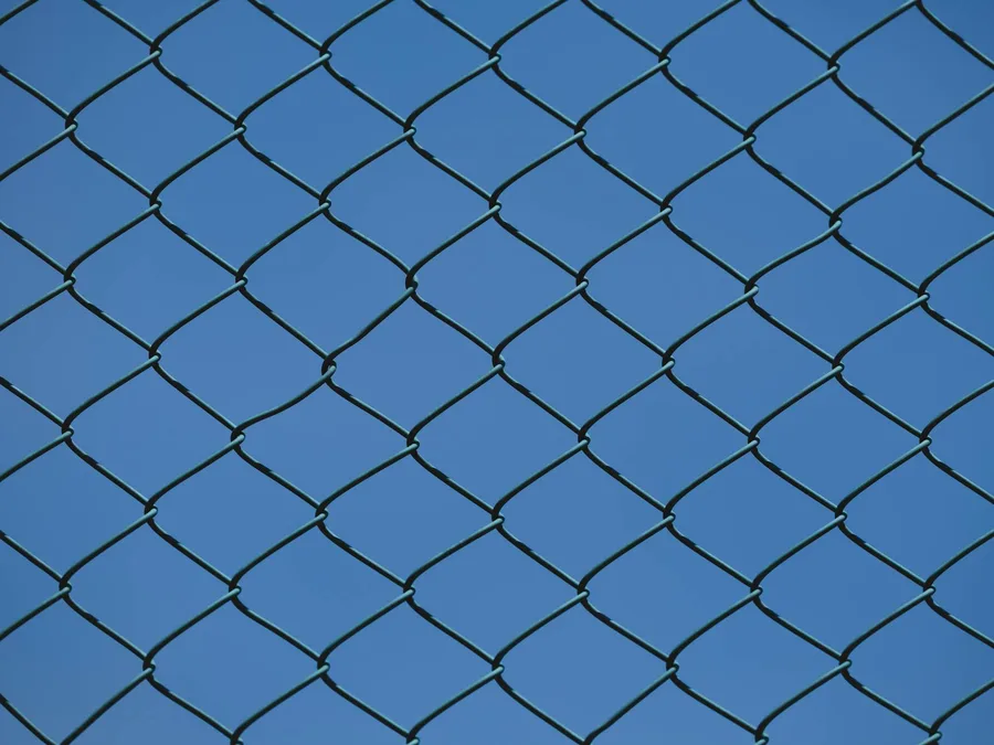 Close-up of a metal chain link fence with clear blue sky in the background, symbolizing urban security and boundaries.
