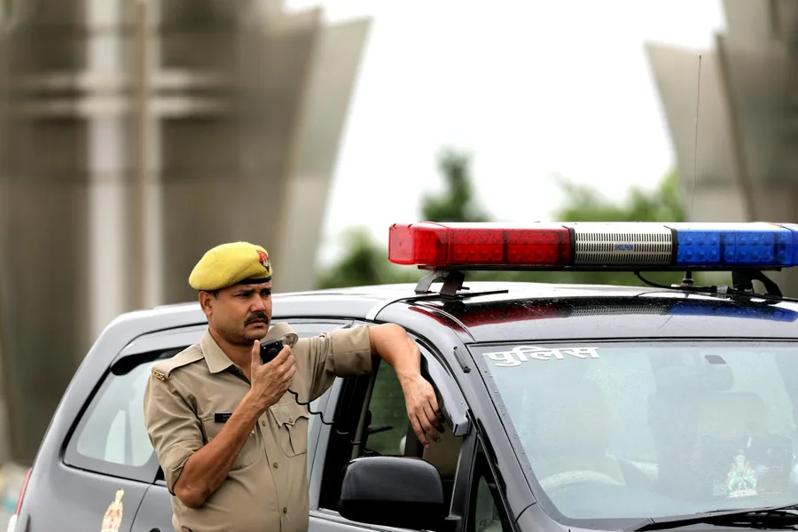Police officer standing beside patrol car holding a radio microphone outdoors.