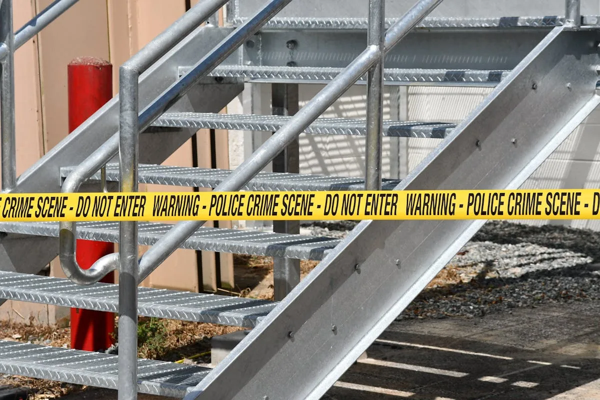 Close-up of a metal stairway blocked by yellow police crime scene tape outdoors.
