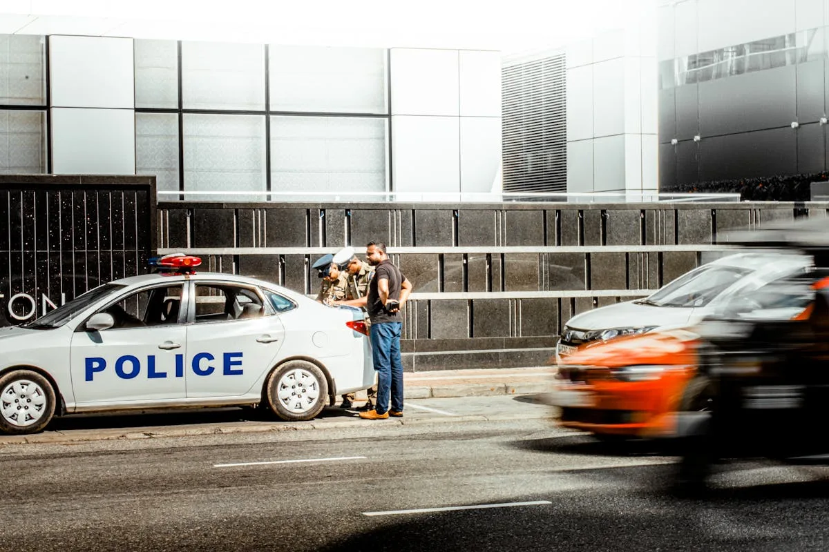 Police officers interacting with a civilian by a street in an urban area.
