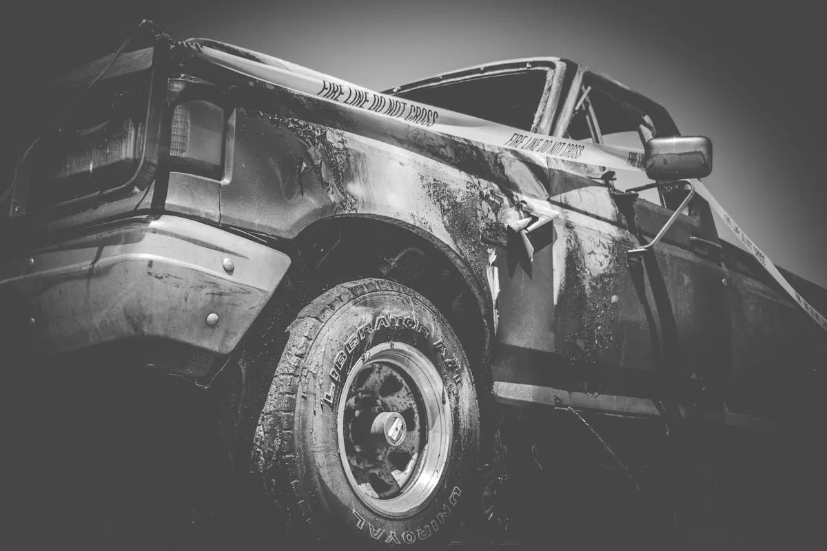 Dramatic black and white image of a damaged truck with police tape.
