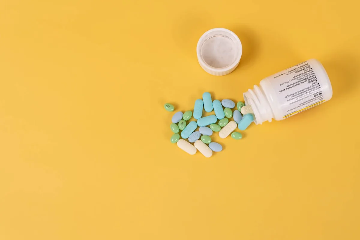 Colorful pills and tablets scattered from an open bottle on a vibrant yellow background. Ideal for healthcare concepts.
