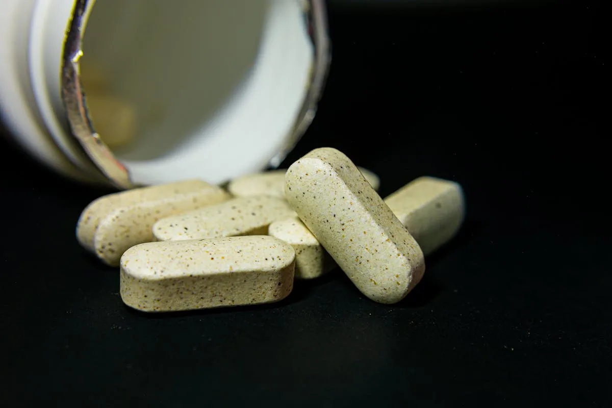 Close-up of white capsule pills spilled from a bottle on a black background. Ideal for health-related visuals.
