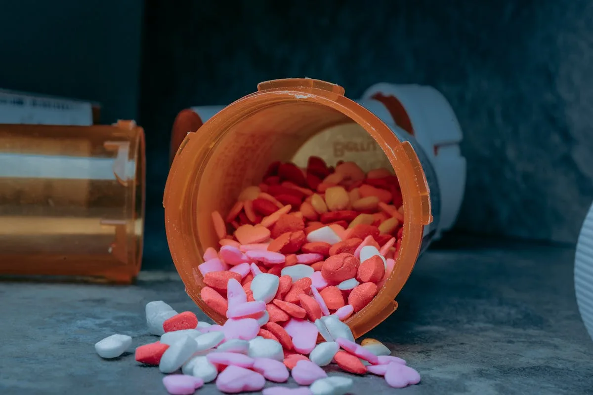 Close-up of heart-shaped pills spilling from a prescription bottle on a surface.
