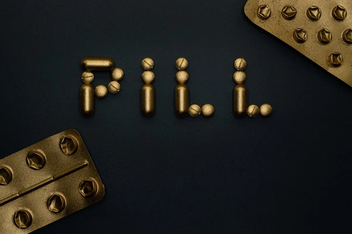 Artistic arrangement of gold pills spelling 'Pill' on a dark backdrop, emphasizing pharmaceutical concepts.

