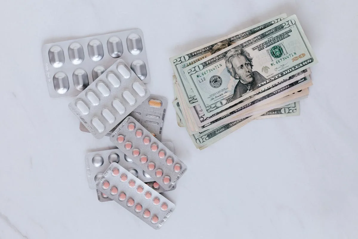 Blister packs of pills and US dollars on a white surface.
