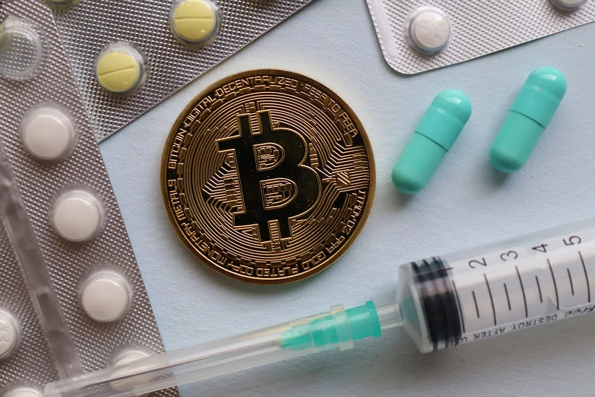 A close-up of a bitcoin, pills, and a syringe, highlighting intersections of finance and healthcare.
