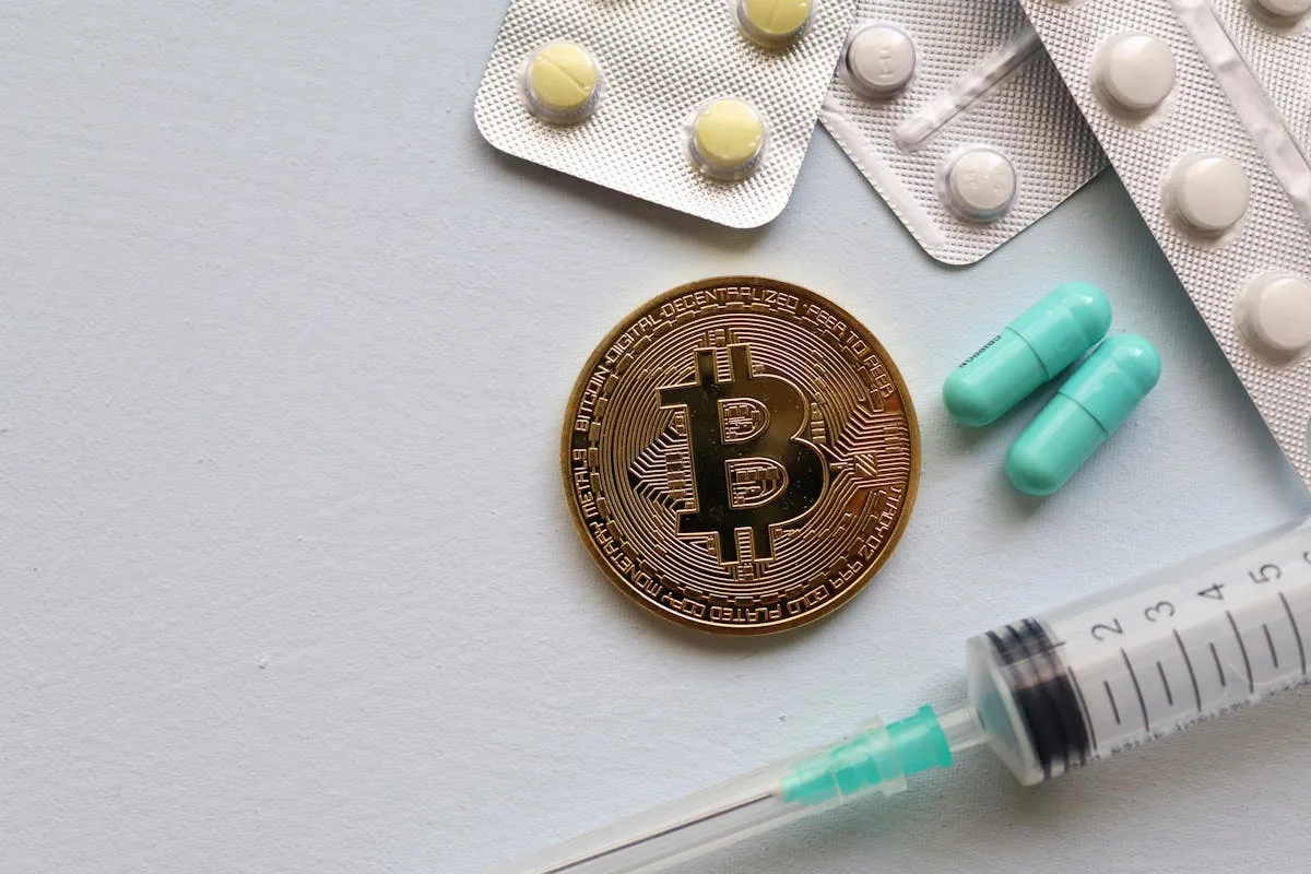 Image of a Bitcoin coin surrounded by pills and a syringe, symbolizing healthcare and finance.