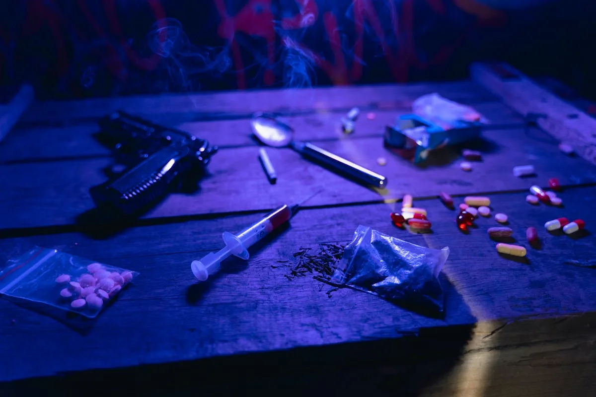 A moody scene displaying drugs, a gun, and smoke under dramatic lighting.
