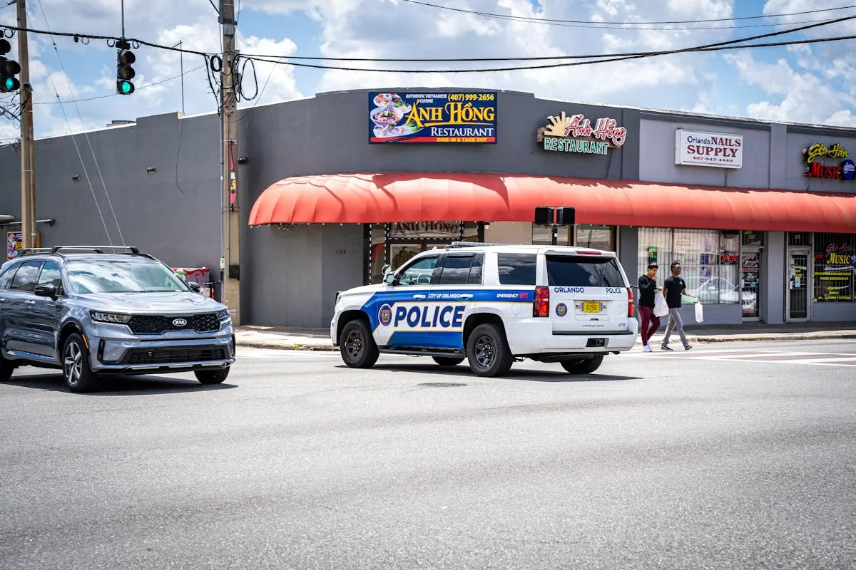 Police vehicle on an Orlando street with traffic and pedestrians under a sunny sky.
