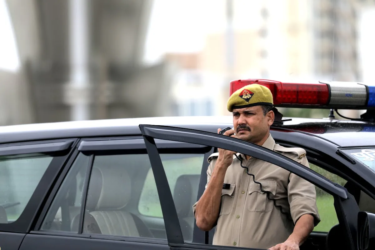 Police officer using radio near patrol car outdoors, ensuring public safety.
