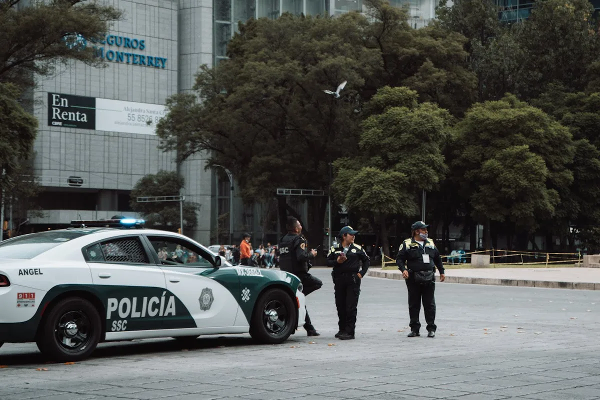 Uniformed police officers stand near patrol car on urban street ensuring public safety.
