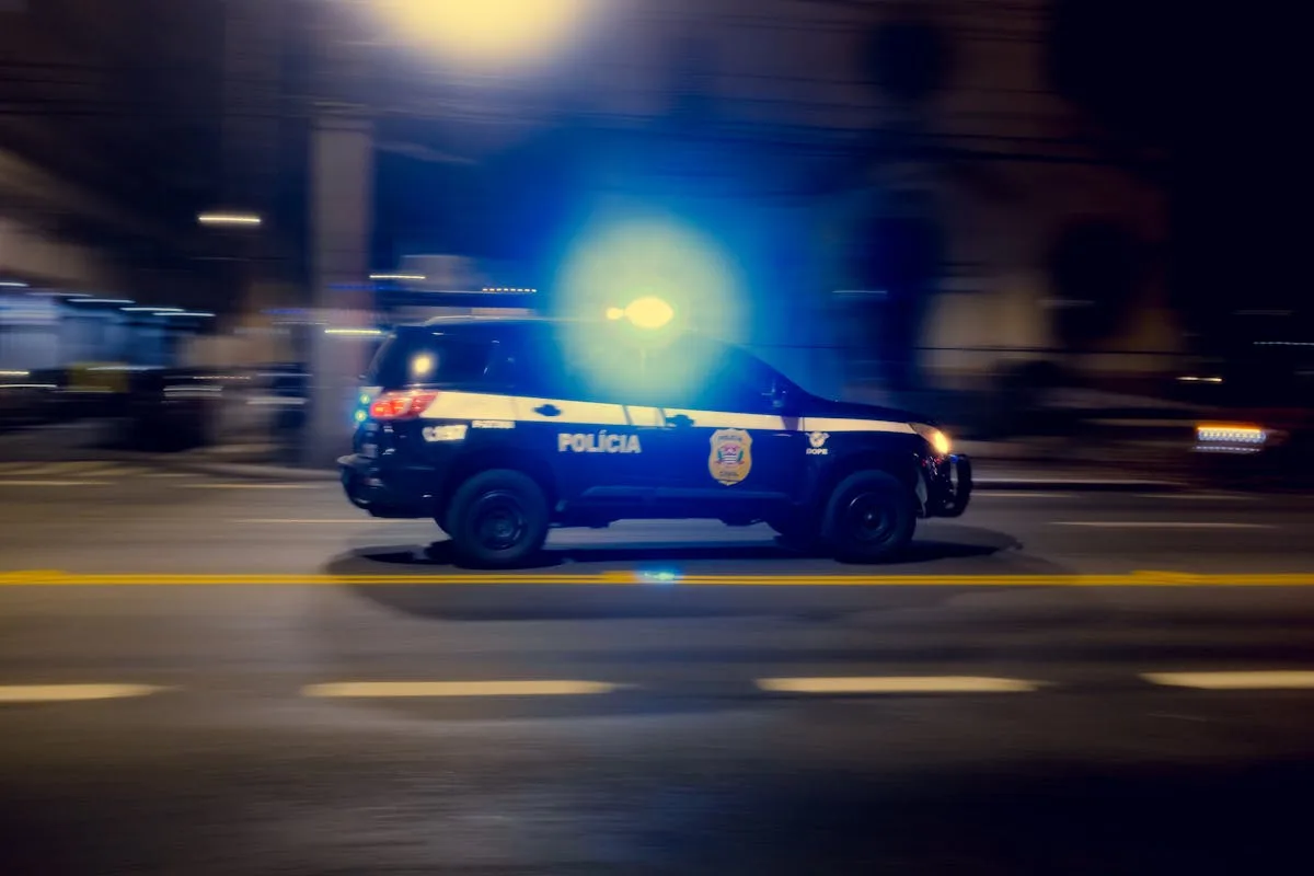 Blurred motion capture of a police car speeding at night with flashing lights on a city street.
