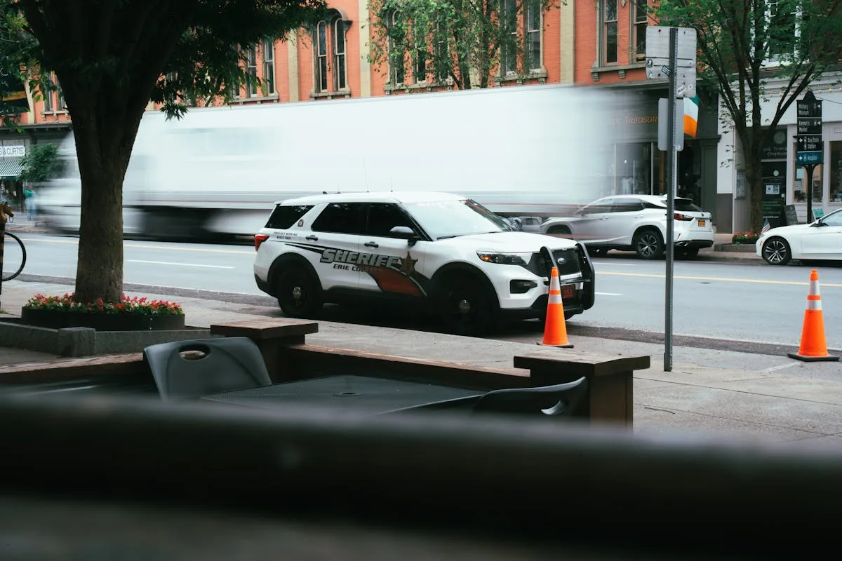 A dynamic urban scene featuring a sheriff police car and blurred traffic in a downtown area.
