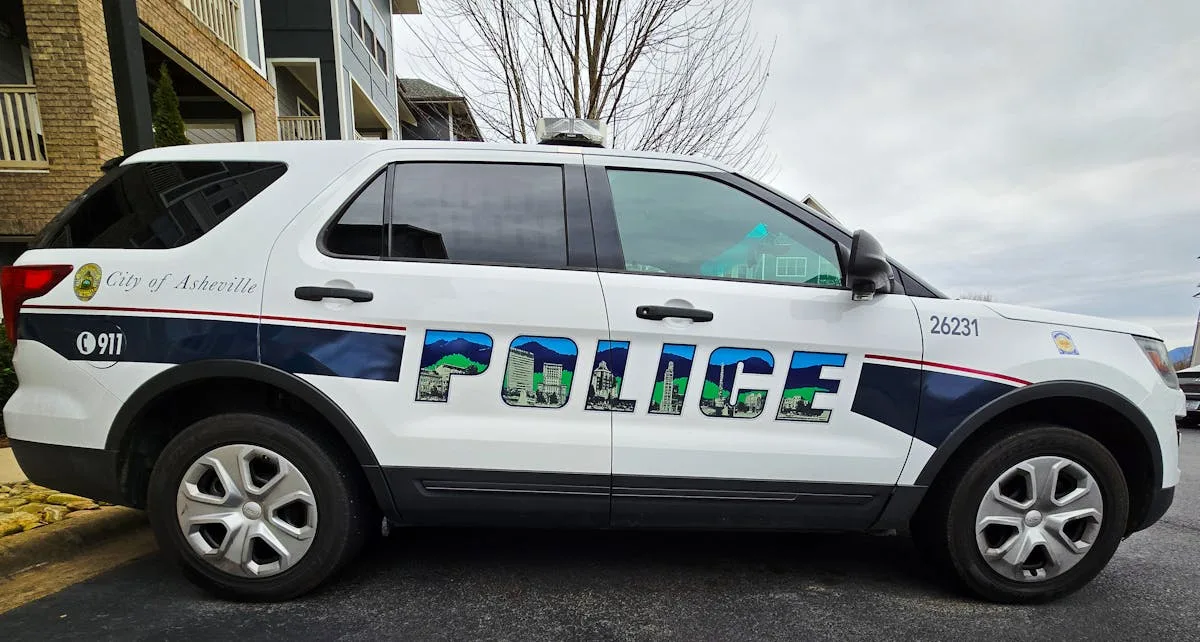 Marked Asheville police SUV parked by residential buildings on a cloudy day.