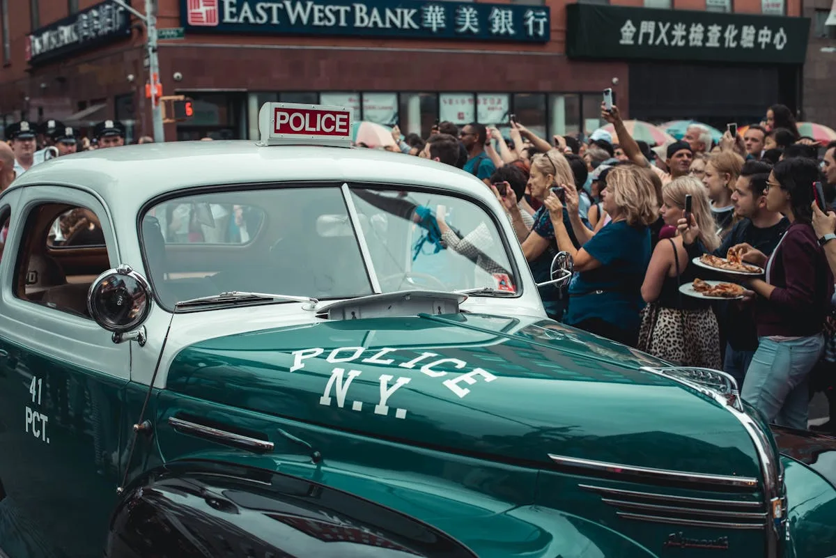 A classic NY police car surrounded by a crowd during a New York City parade.