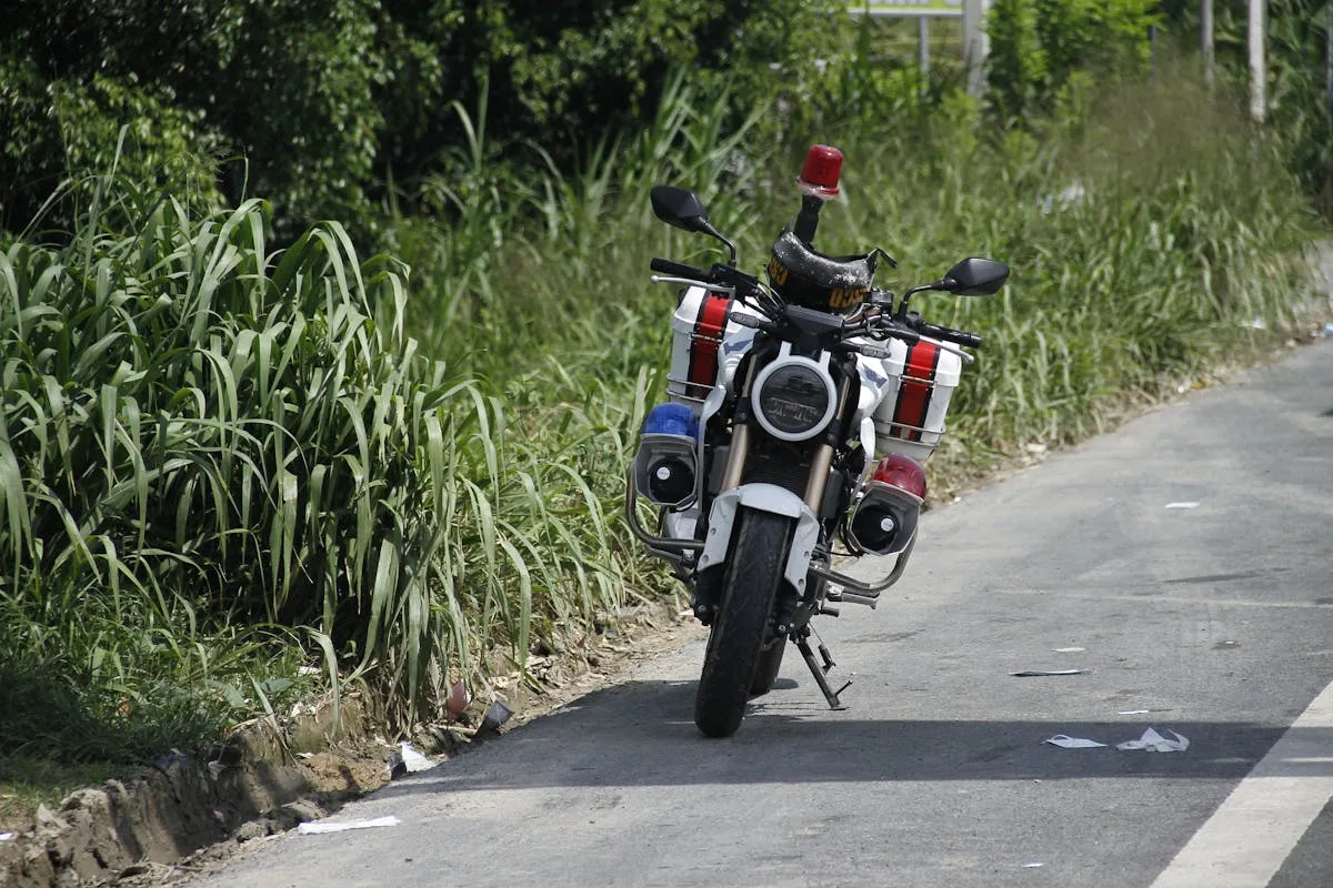 A police motorcycle stands parked by a rural roadside, surrounded by lush greenery.