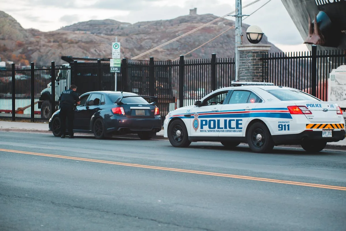 Back view of unrecognizable police officer in uniform checking modern car parked on asphalt road against cloudy sky
