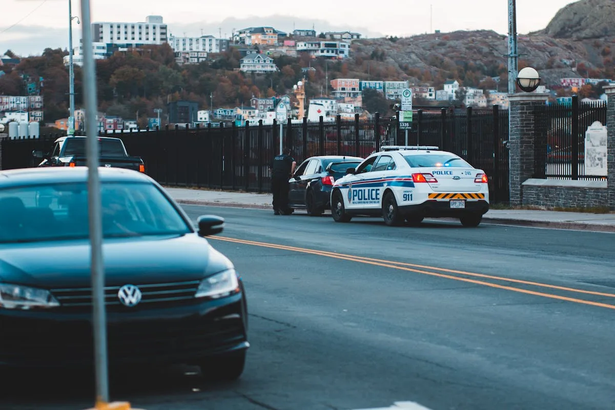 Police car patrolling urban street with city buildings in the background during twilight.
