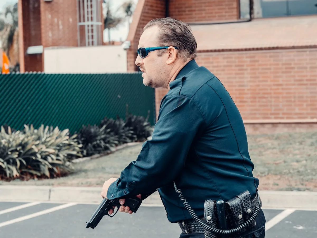 A focused police officer in uniform holding a gun outdoors, depicting law enforcement in action.
