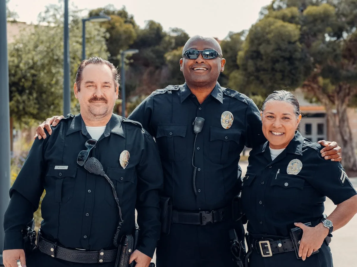 Three police officers in uniform smiling together outdoors, symbolizing community and law enforcement.
