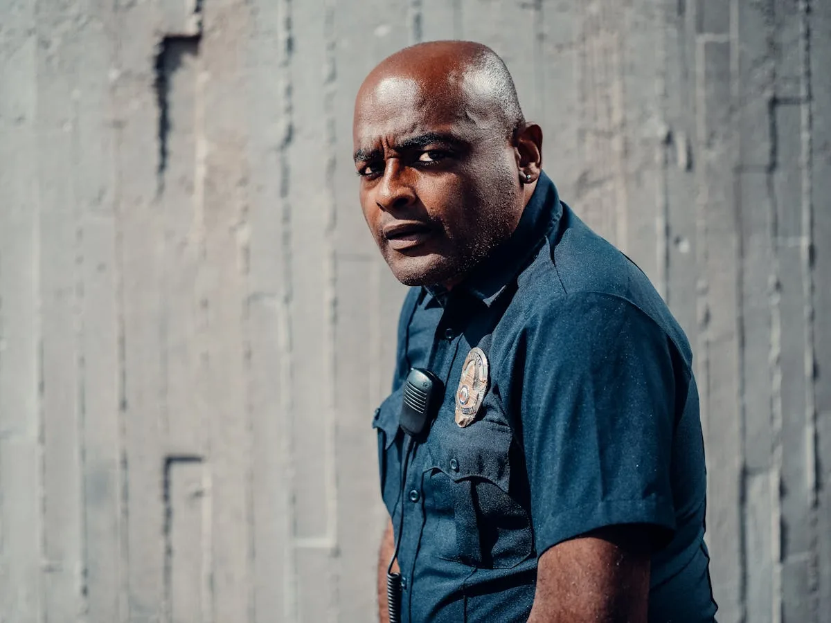 A police officer in uniform standing confidently outdoors, looking sideways, conveying authority.
