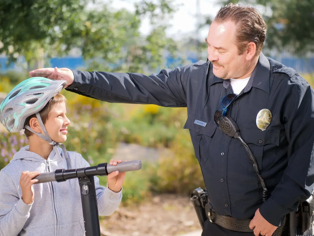 A police officer helps a child adjust his helmet while riding a scooter in a community park.