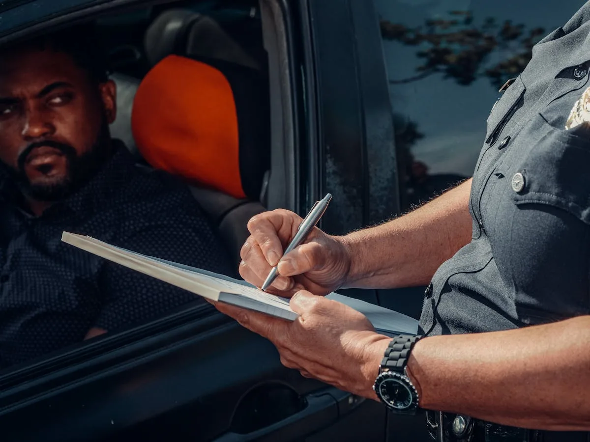 A police officer writes a ticket as the driver looks on from inside the car.