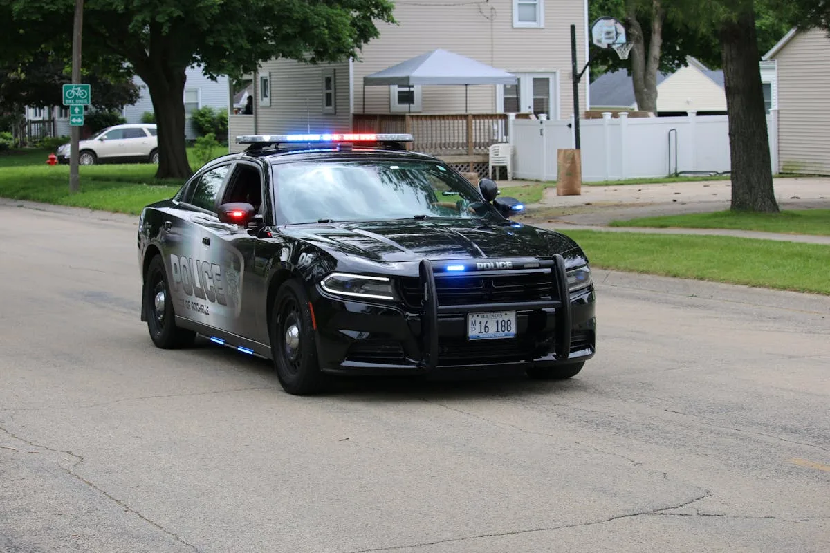 A police car drives through an urban neighborhood street during the day.

