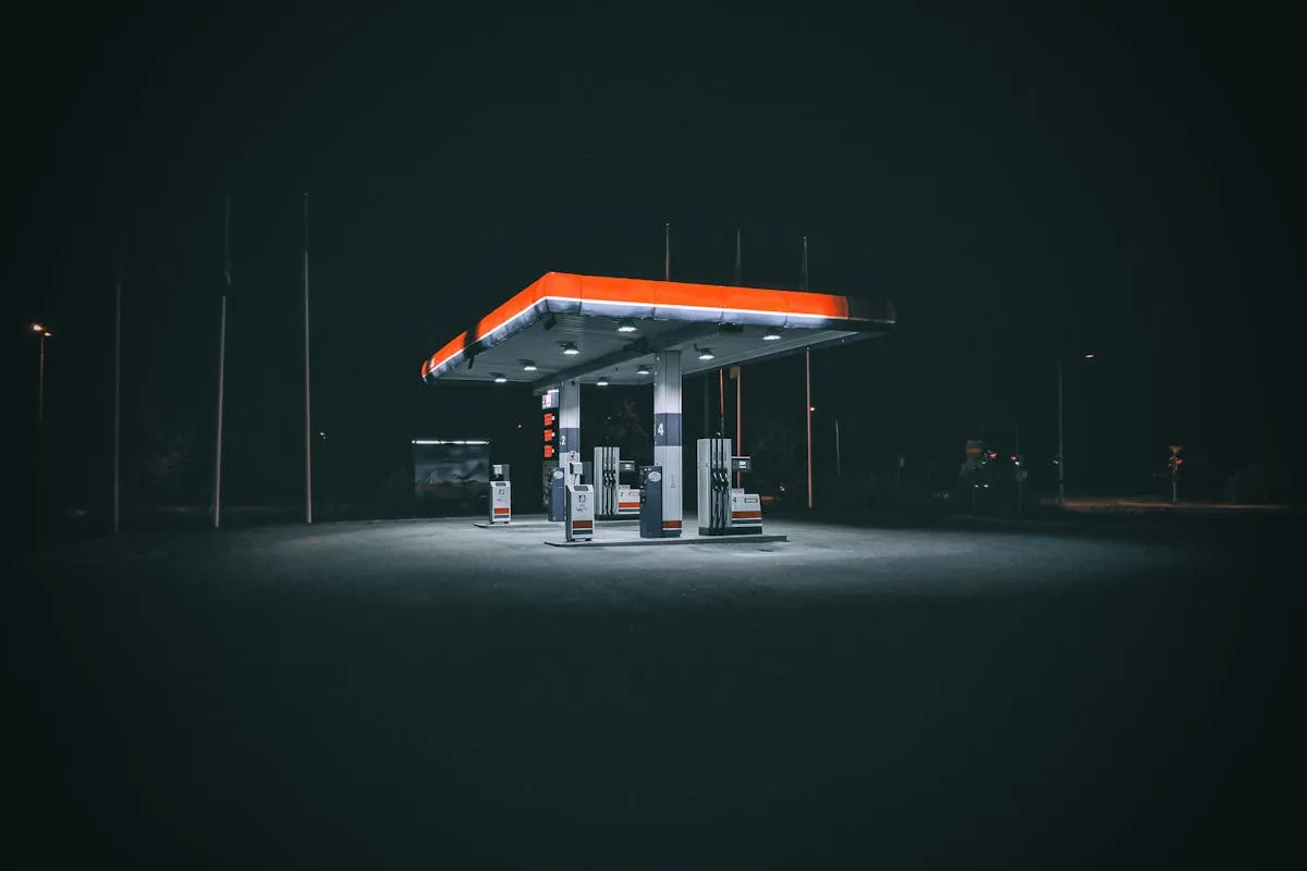An isolated and illuminated gas station at night, highlighting urban solitude under a dark sky.

