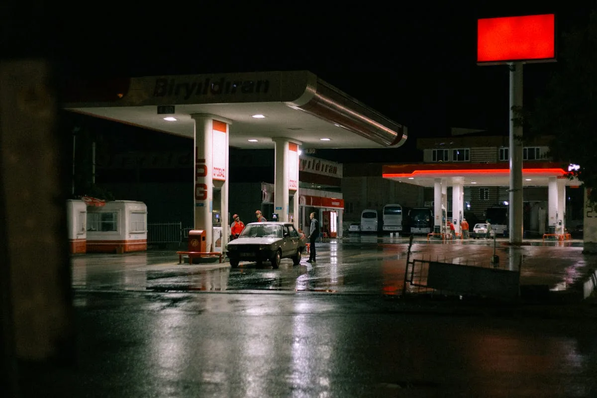 A car and people at a brightly lit gas station during the night.